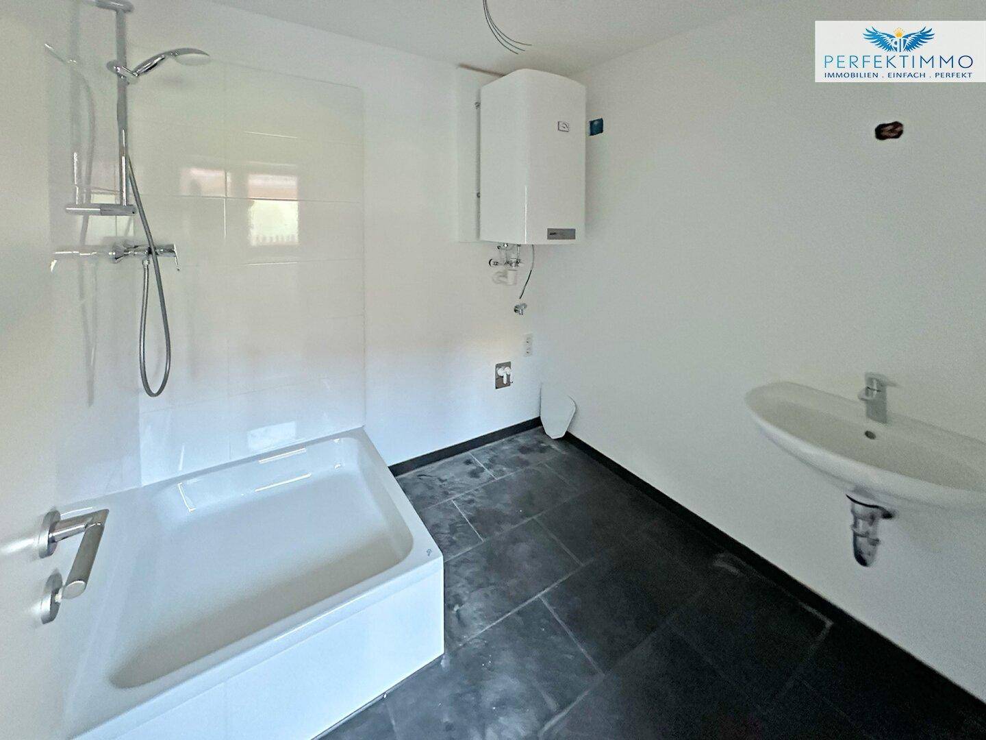 Modernisiertes Badezimmer mit Badewanne, Dusche und Waschbecken, dunklen Bodenfliesen.