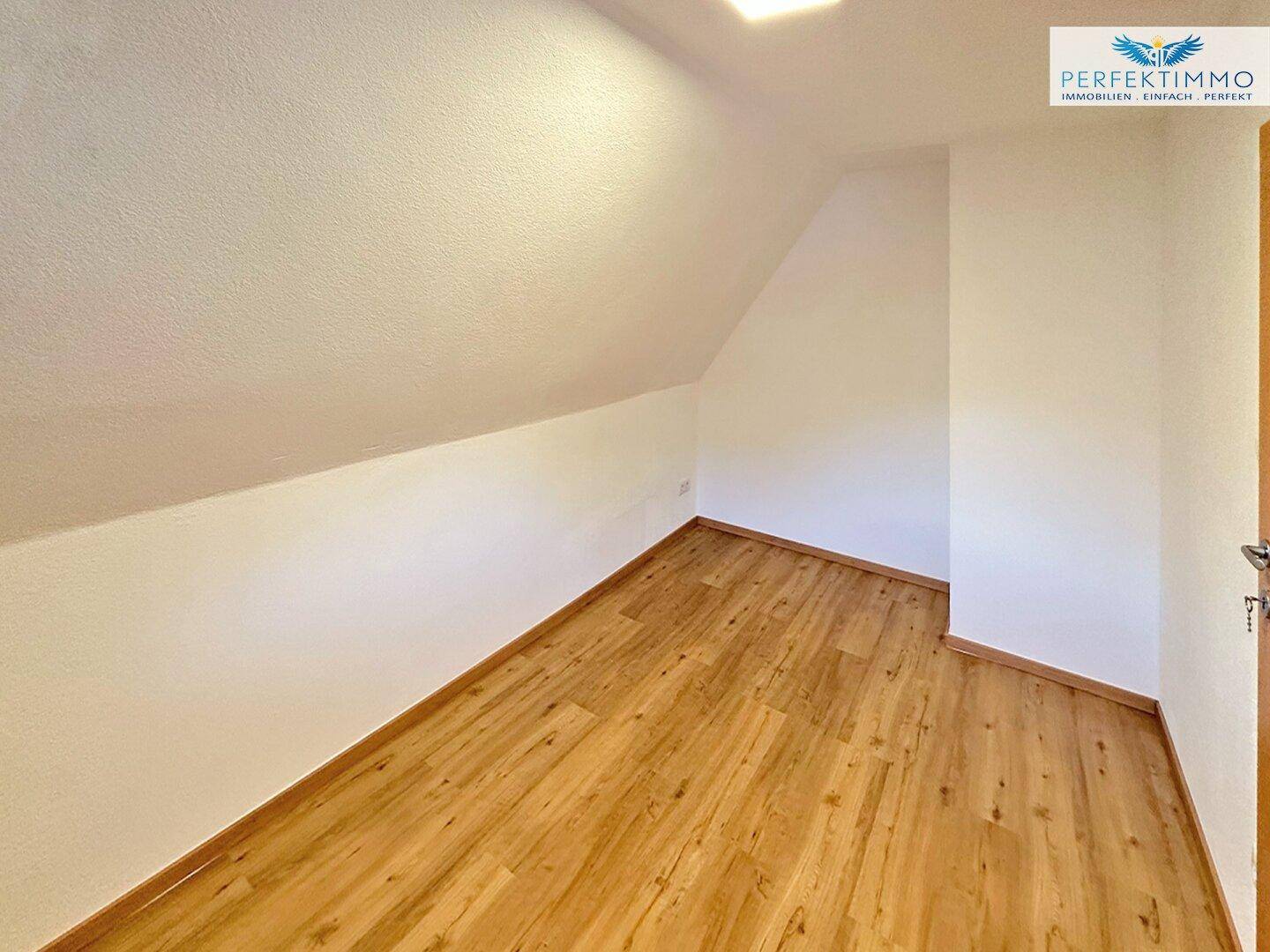 Schlafzimmer im Dachgeschoss mit Laminatboden, weißen Wänden und Dachschräge.