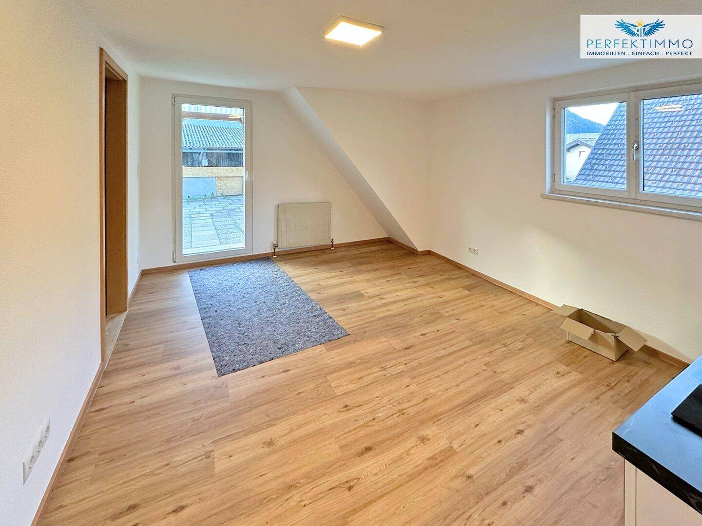 Heller Wohnraum mit Laminatboden, Dachschräge und Zugang zu einem Außenbereich.