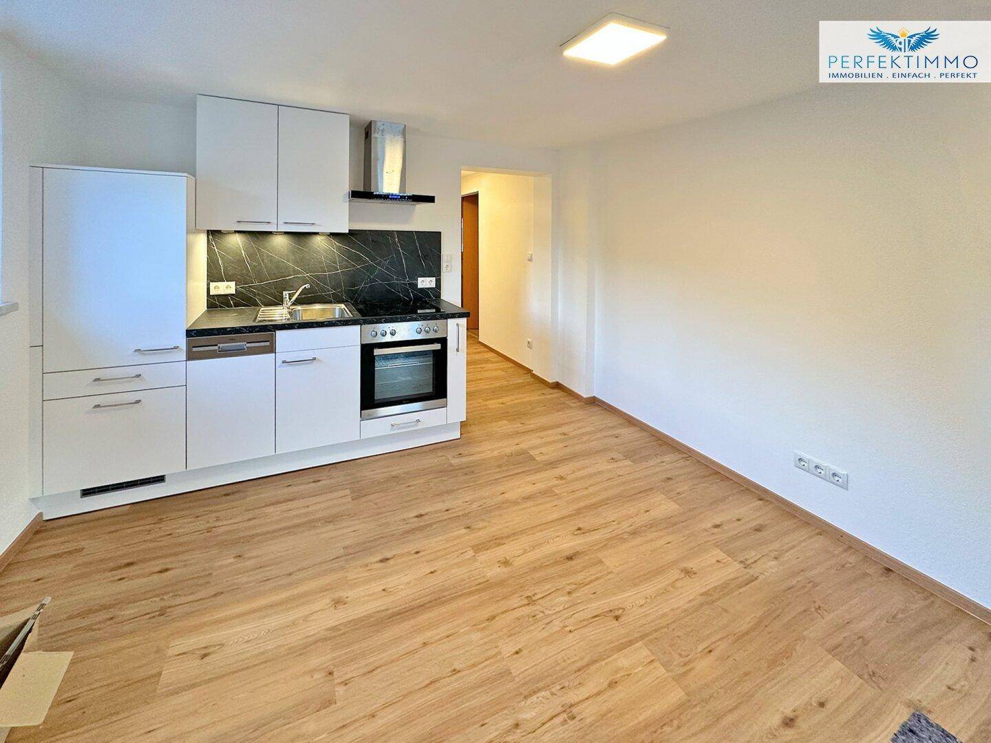 Offene Küche mit weißen Schränken, dunkler Arbeitsplatte und Laminatboden.