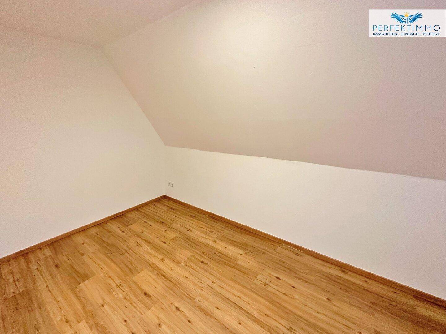Schlafzimmer im Dachgeschoss mit Laminatboden, weißen Wänden und Dachschräge.