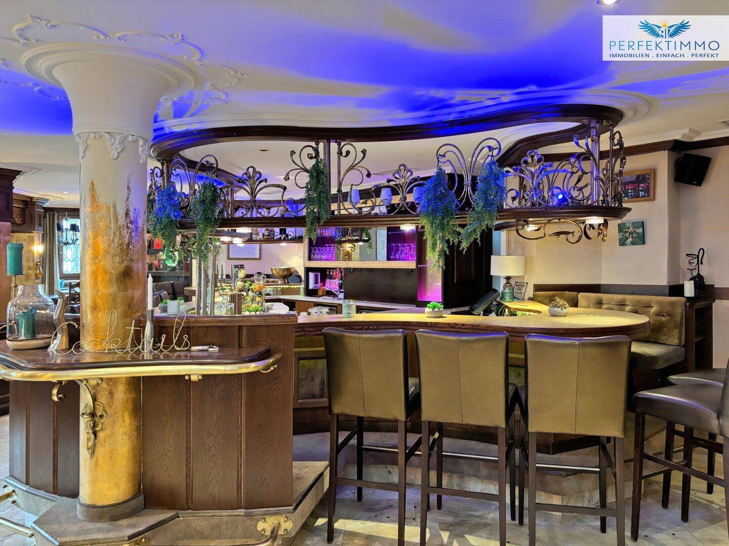 Stilvolle Bar mit runder Theke, hohen Hockern und dekorativer Beleuchtung.