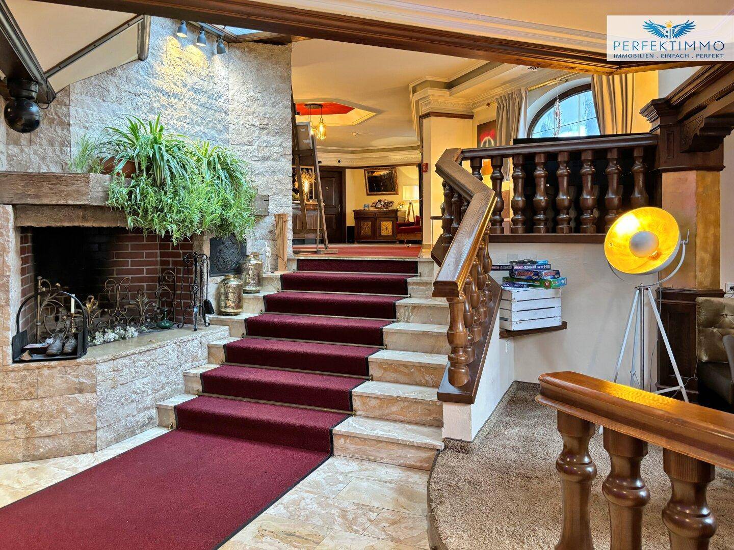 Elegante Lobby mit großem Kamin, Teppichtreppe und traditionellem Holzgeländer.