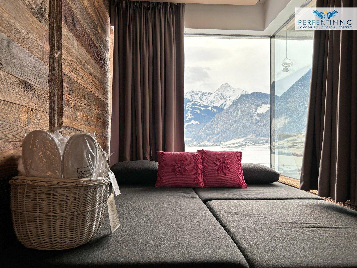 Gemütlicher Liegebereich mit Blick auf die schneebedeckten Berge durch große Fenster.