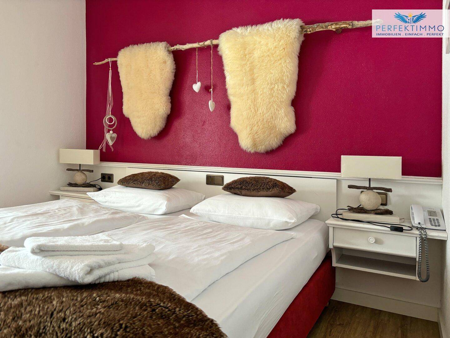 Schlafzimmer mit lebendiger magentafarbener Akzentwand und rustikaler Dekoration über dem Bett.