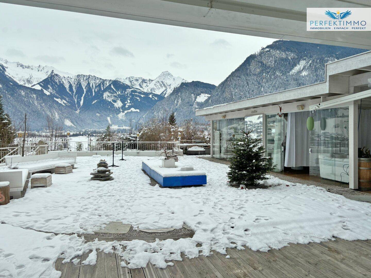 Weitläufige Außenterrasse mit Schnee bedeckt, umgeben von einer beeindruckenden Berglandschaft.