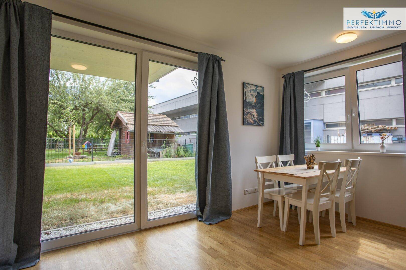 Essbereich mit Holztisch und Stühlen, großen Fenstern und Blick auf den Garten.