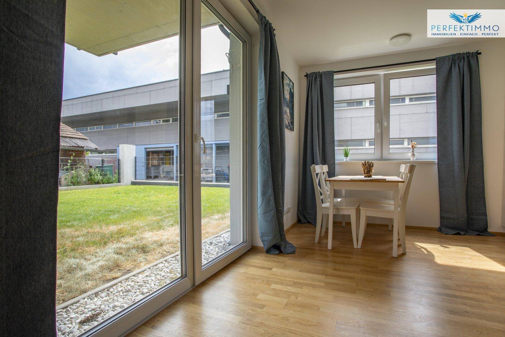 Heller Wohnbereich mit großen Fenstern, die einen direkten Zugang zum Garten bieten.