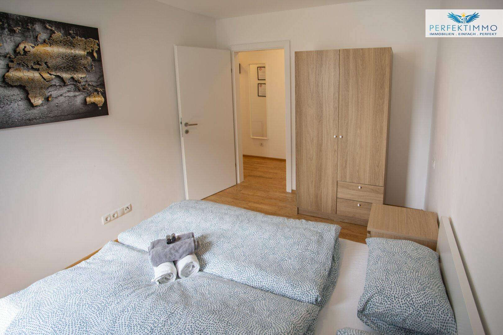 Gemütliches Schlafzimmer mit Doppelbett, Kleiderschrank und Holzboden.