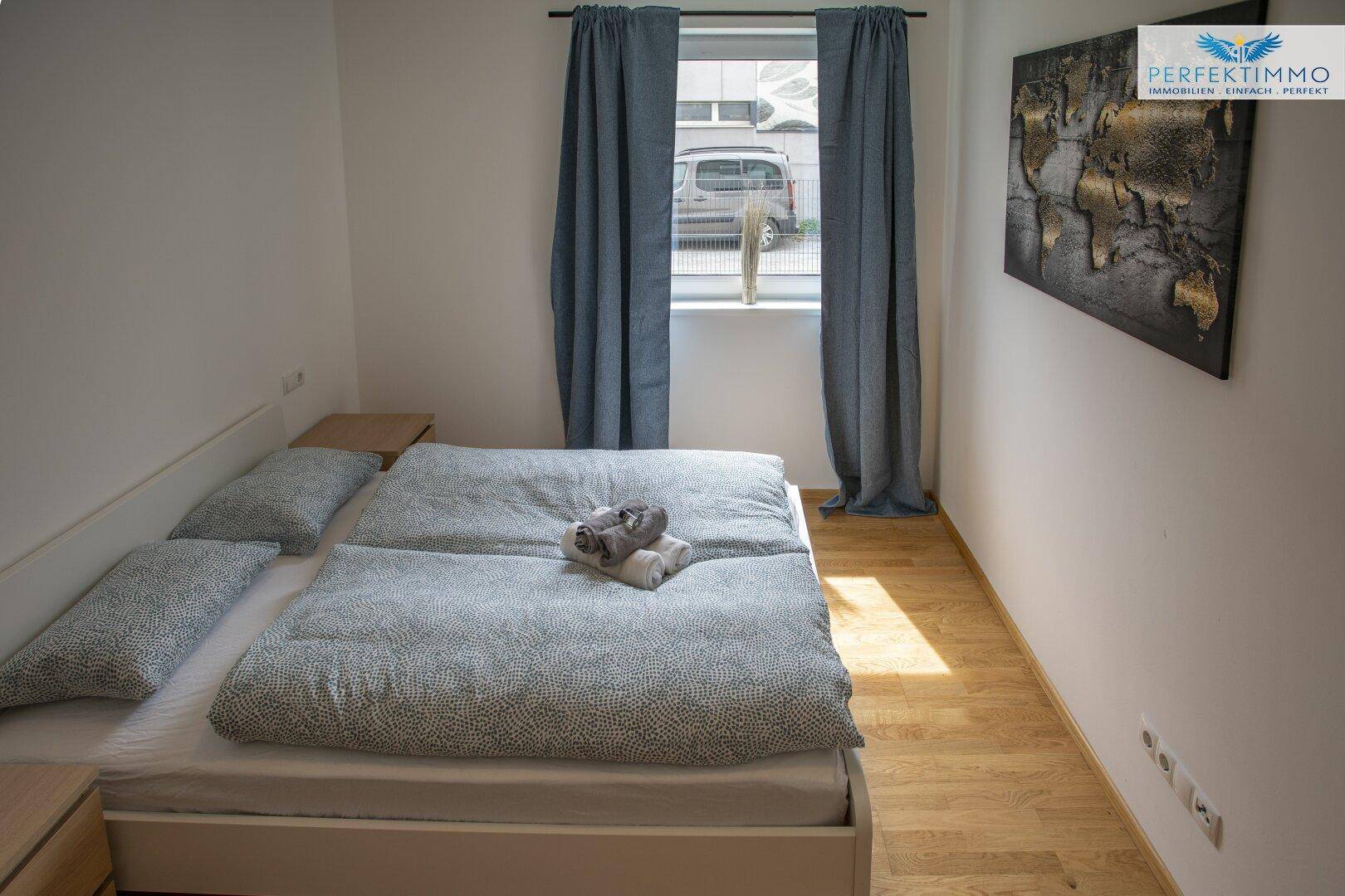 Helles Schlafzimmer mit Doppelbett und Fenster, das Tageslicht hereinlässt.