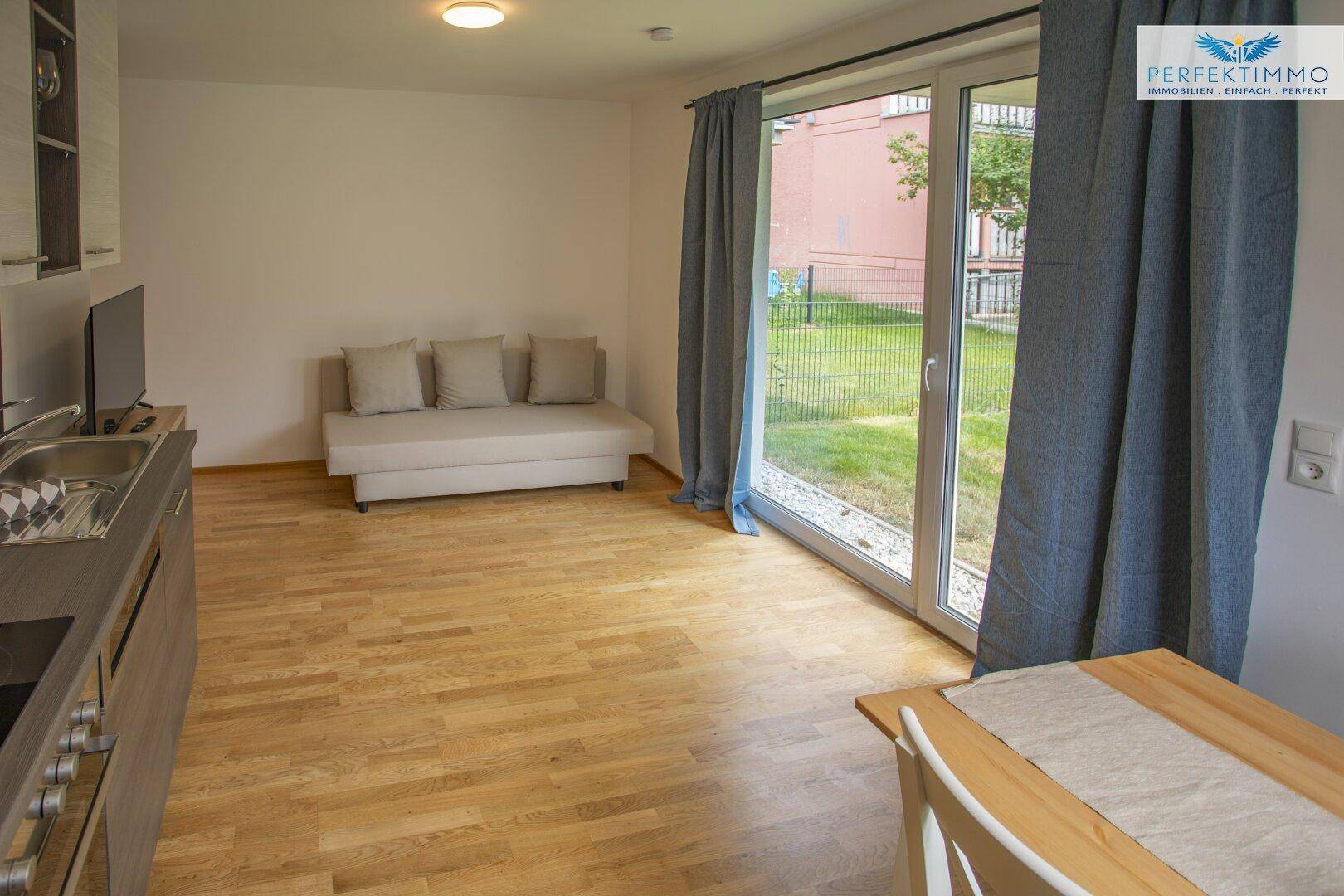 Heller Wohnbereich mit Sofa und Zugang zu einem kleinen Garten.