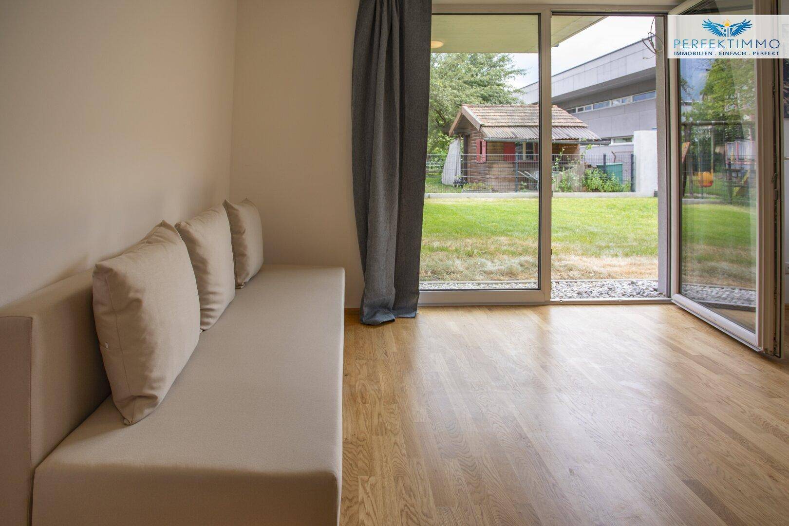 Gemütlicher Wohnbereich mit Sofa und großen Fenstern zum grünen Außenbereich.