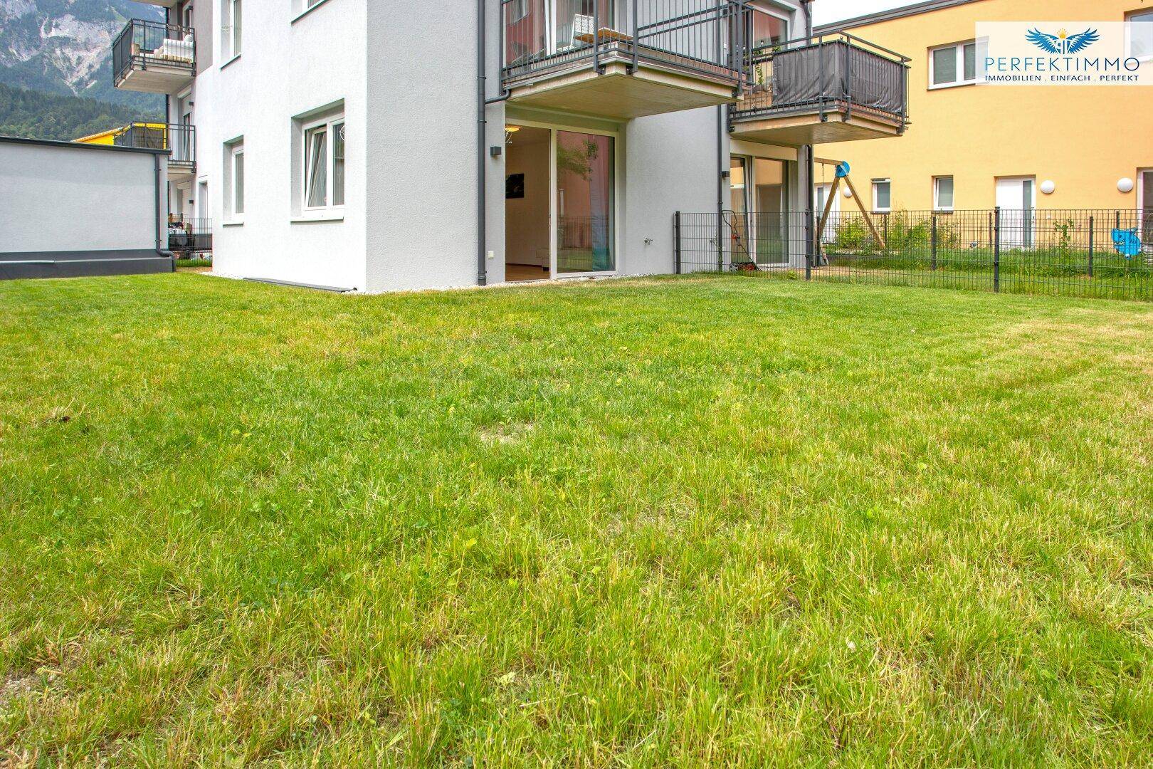 Gepflegte Rasenfläche vor dem Gebäude mit Balkonen und Zugang zum Garten.