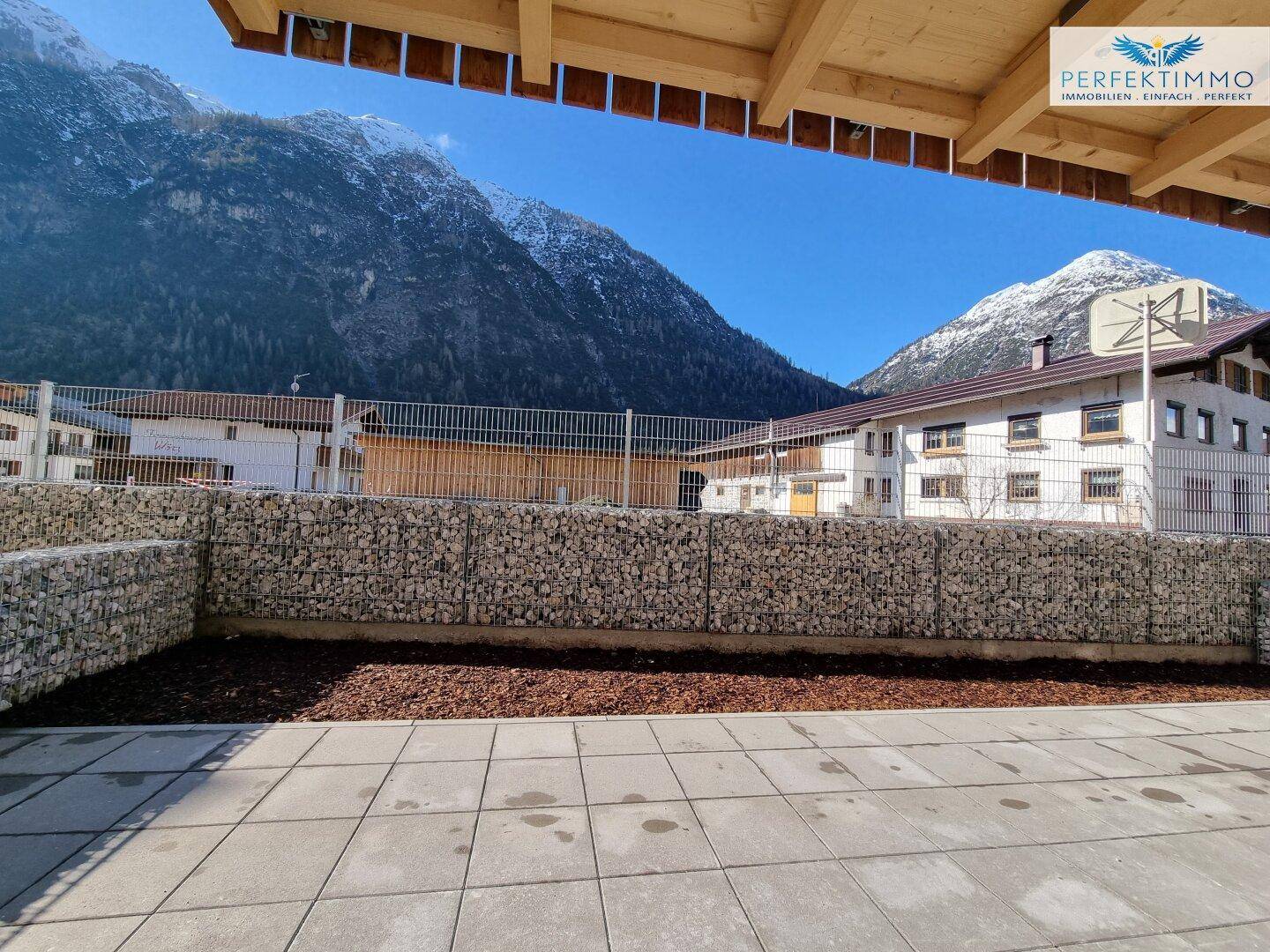 Gepflasterte Terrasse mit Gabionenmauer und beeindruckendem Bergblick in sonniger Lage.