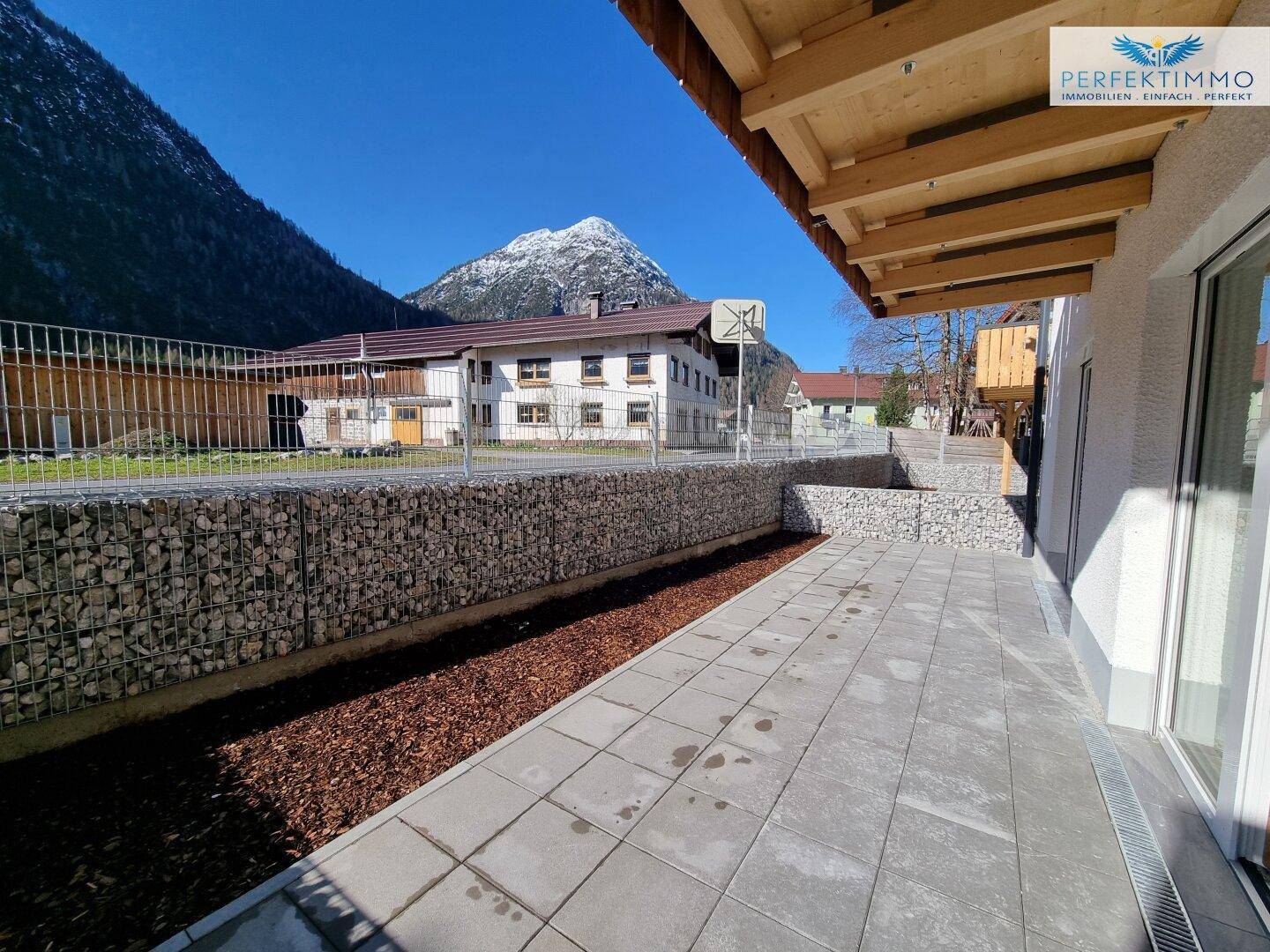 Weitläufige Terrasse mit Gabionenbegrenzung und freiem Blick auf die umliegende Berglandschaft.