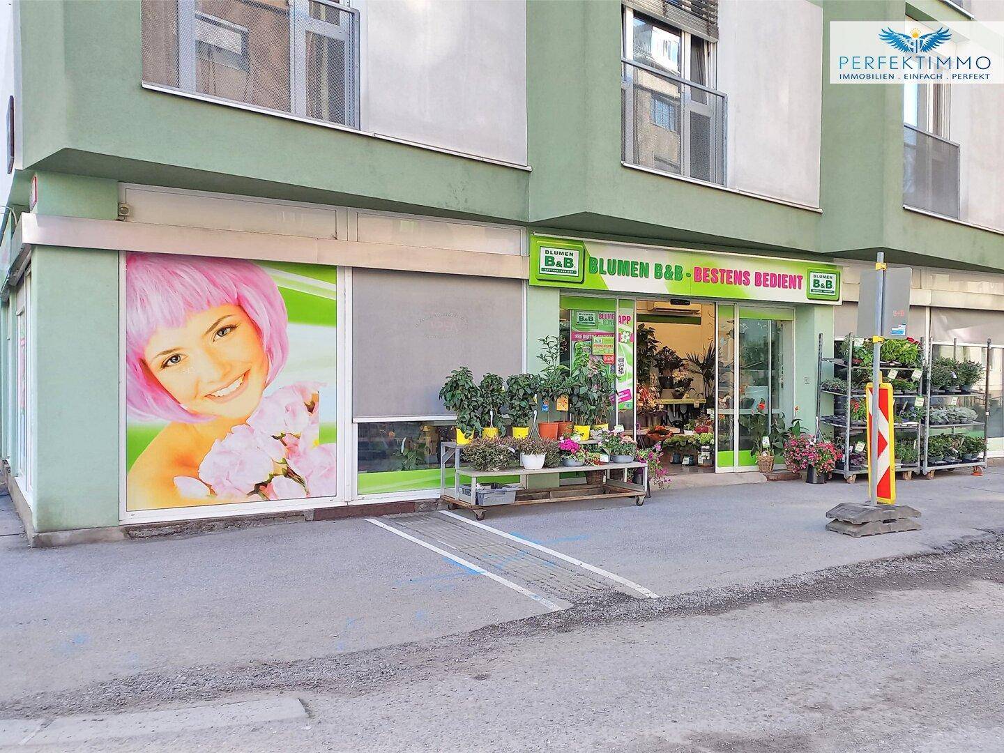 Außenansicht eines Blumengeschäfts im Erdgeschoss eines modernen Gebäudes mit Pflanzen vor dem Eingang.