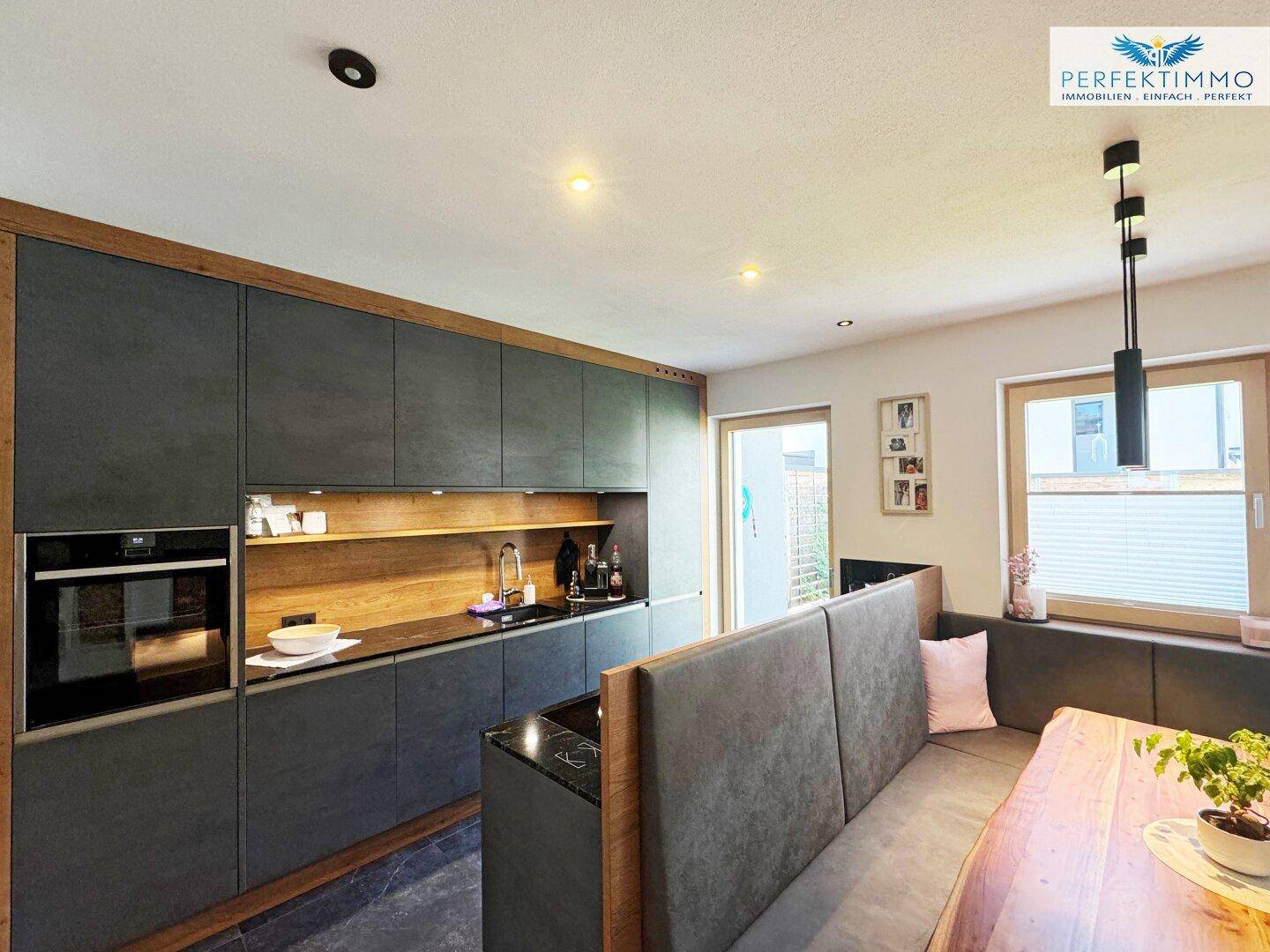 Moderne Wohnküche mit dunklen Schränken, Holzakzenten und integriertem Essbereich.