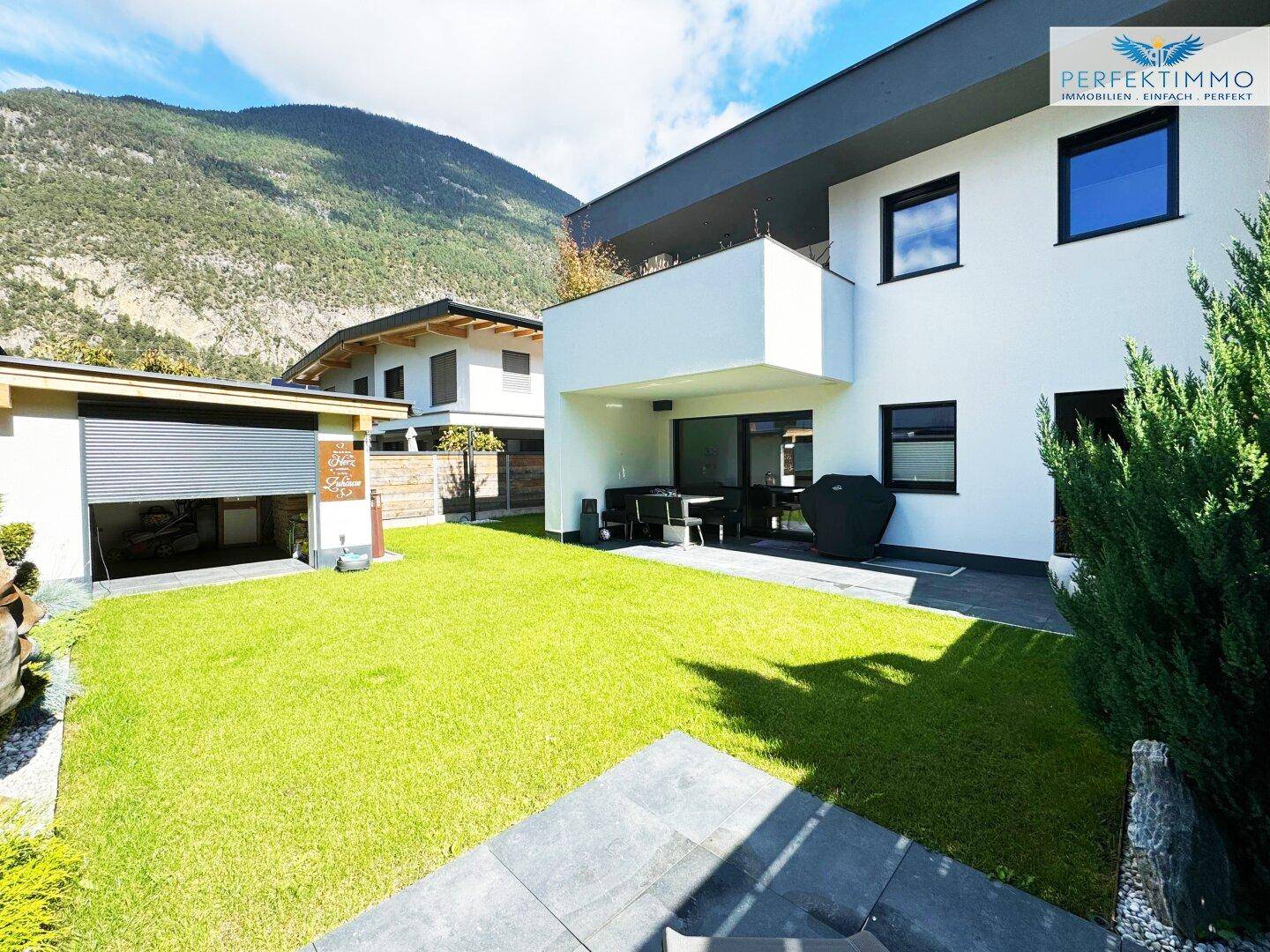 Gepflegter Gartenbereich mit Rasenfläche, Terrasse und Blick auf die Berge.