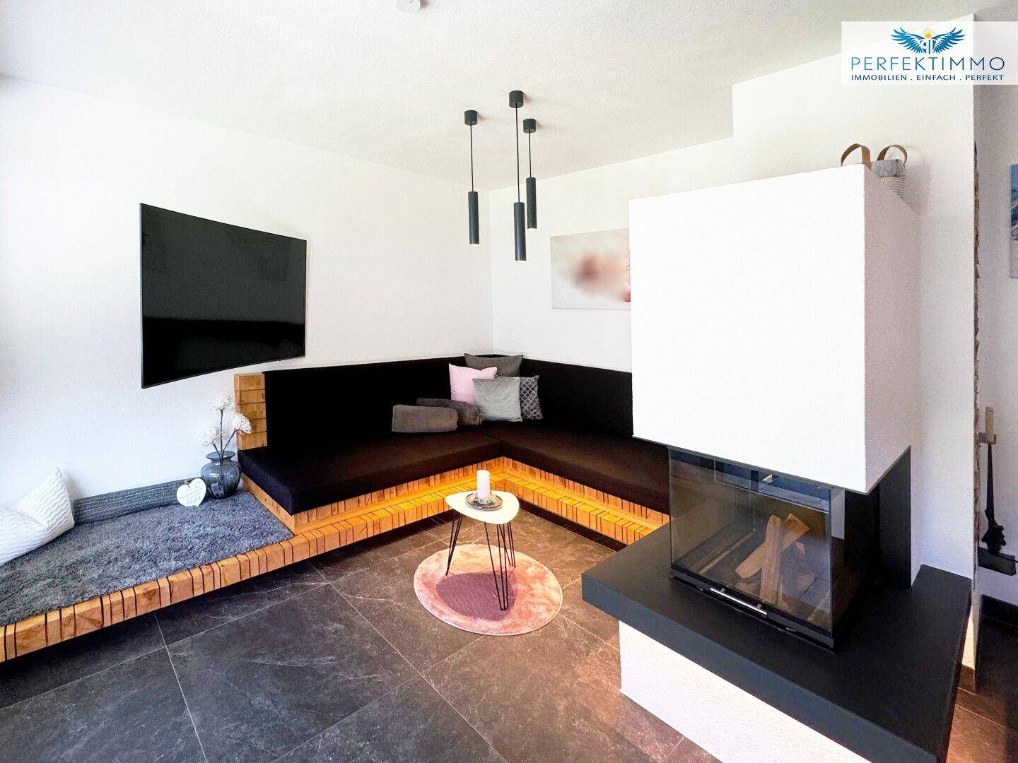 Gemütliches Wohnzimmer mit integriertem Kamin, Ecksofa und dunklem Fliesenboden.