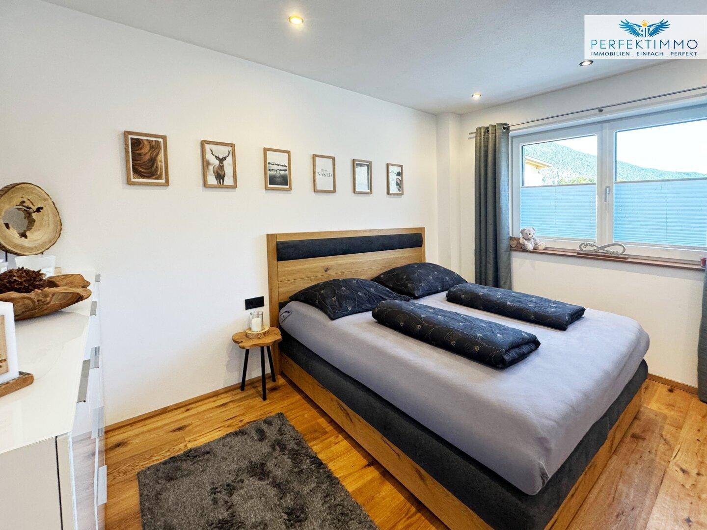 Helles Schlafzimmer mit Holzboden, großem Bett und Blick ins Grüne.