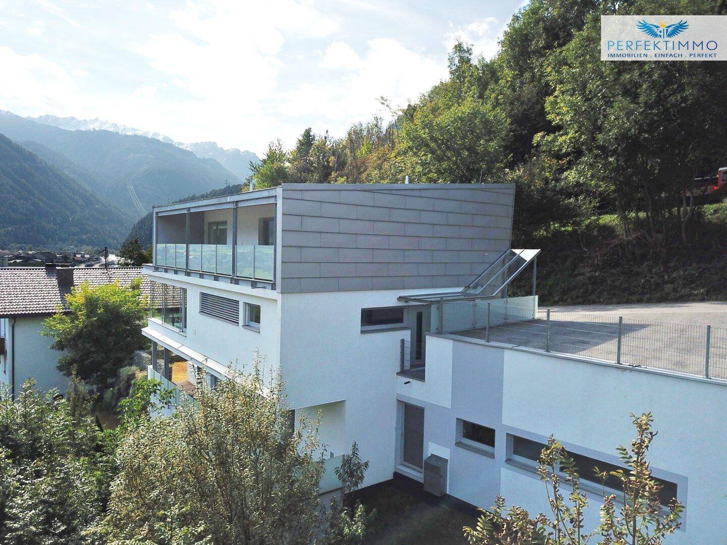Moderne Architektur des Gebäudes mit mehreren Balkonen und einer beeindruckenden Bergkulisse.