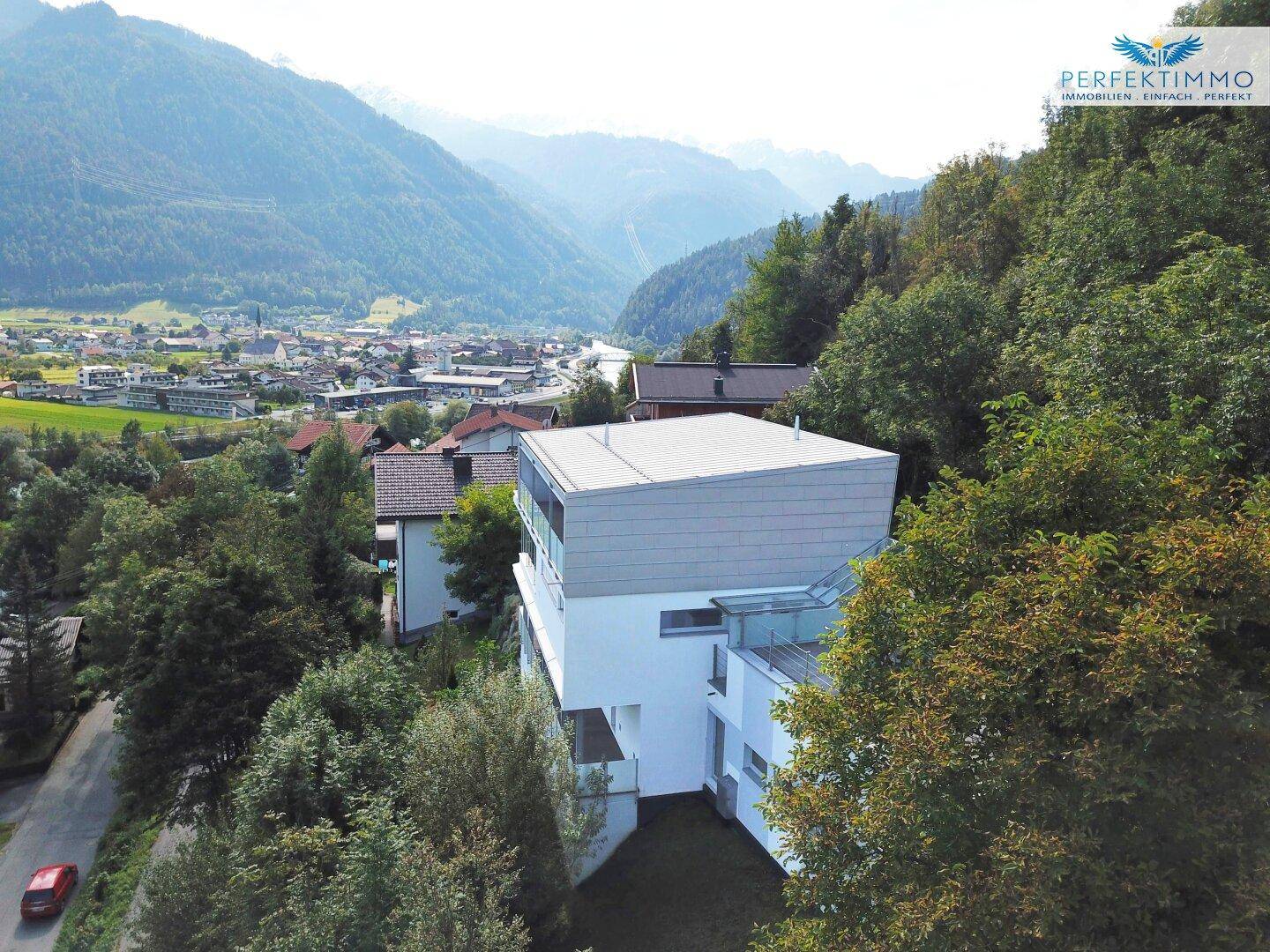 Luftaufnahme des modernen Gebäudes, eingebettet in eine grüne Hügellandschaft mit Bergblick.