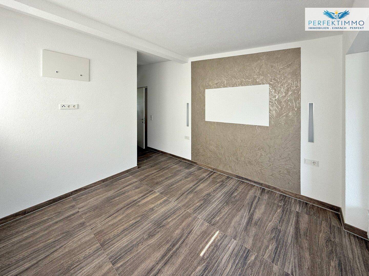 Geräumiger Raum mit Holzbodenfliesen und einer strukturierten Akzentwand, bereit zur individuellen Gestaltung.