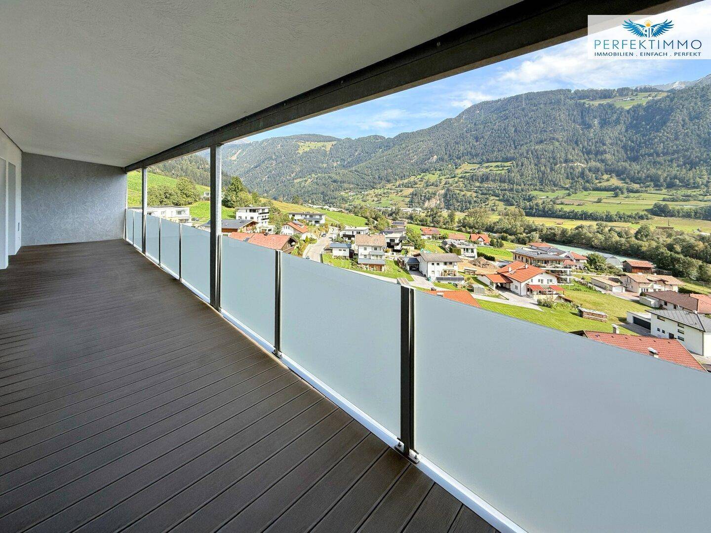 Geräumiger Balkon mit Holzboden und Glasbrüstung bietet einen weiten Blick auf die Berglandschaft.