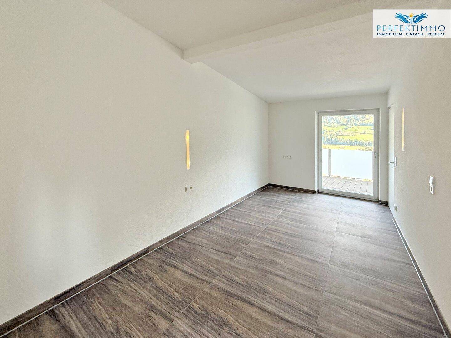 Heller Raum mit Holzbodenfliesen und Zugang zu einem Balkon oder einer Terrasse mit Bergblick.