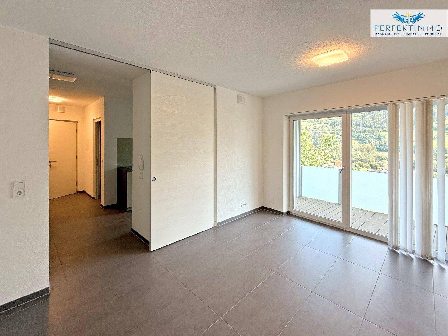 Heller Wohnbereich mit Fliesenboden, Schiebetür und Zugang zu einem Balkon mit Bergblick.