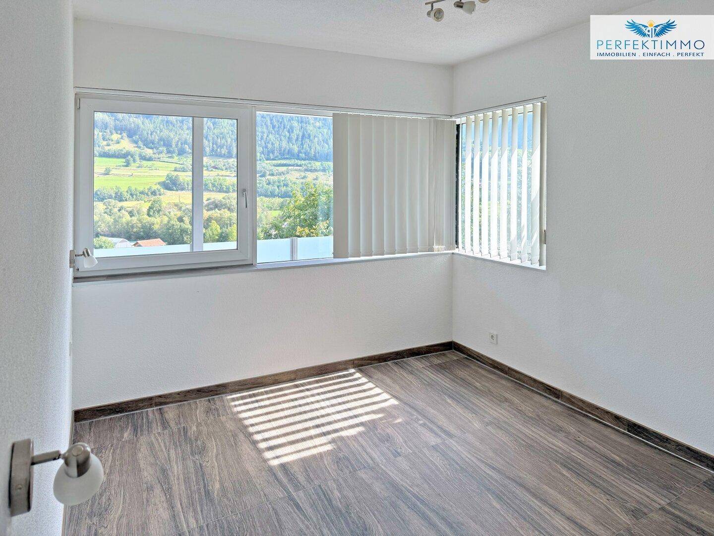 Helles Schlafzimmer mit großen Fenstern, die einen weiten Blick auf die grüne Landschaft bieten.