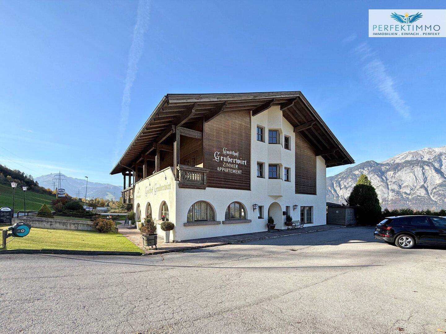 Traditionelles Gasthaus mit alpiner Architektur und Bergblick unter blauem Himmel.