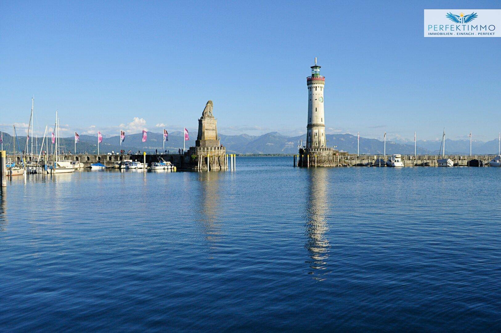 Historischer Hafen mit Leuchtturm und Statue, umgeben von Segelbooten und einer beeindruckenden Bergkulisse.