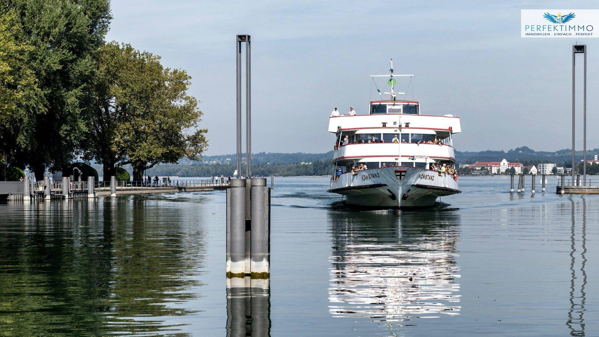 Ein Passagierschiff fährt auf dem See, umgeben von grünen Ufern und einer malerischen Landschaft.