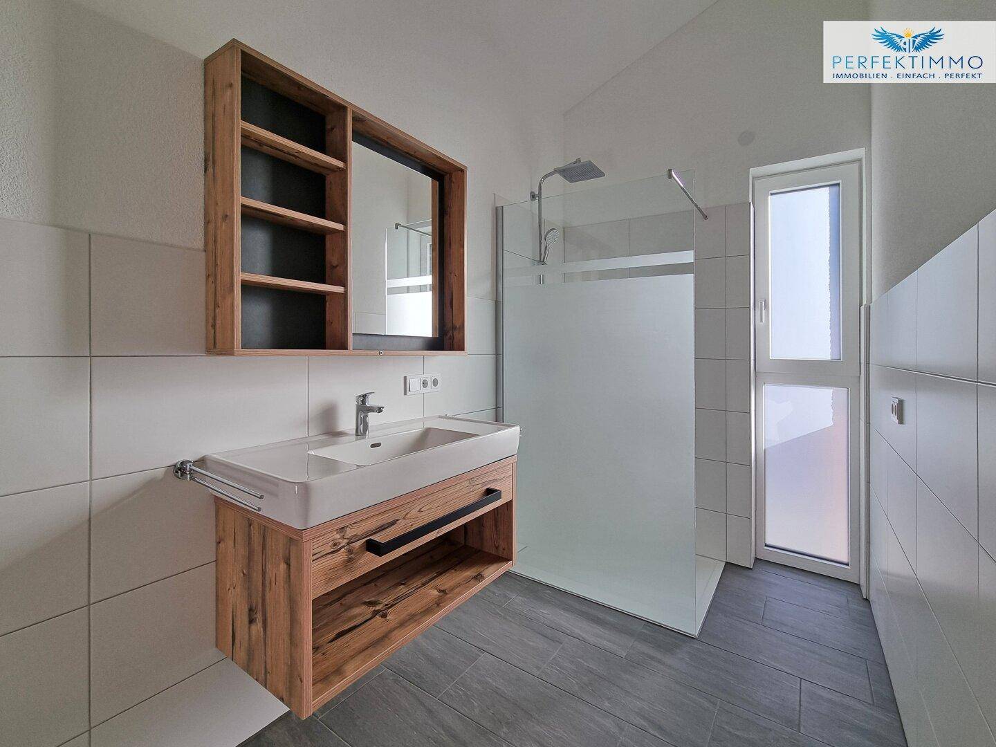 Modernes Badezimmer mit begehbarer Dusche, Fenster und Holzwaschtisch, hell und funktional gestaltet.