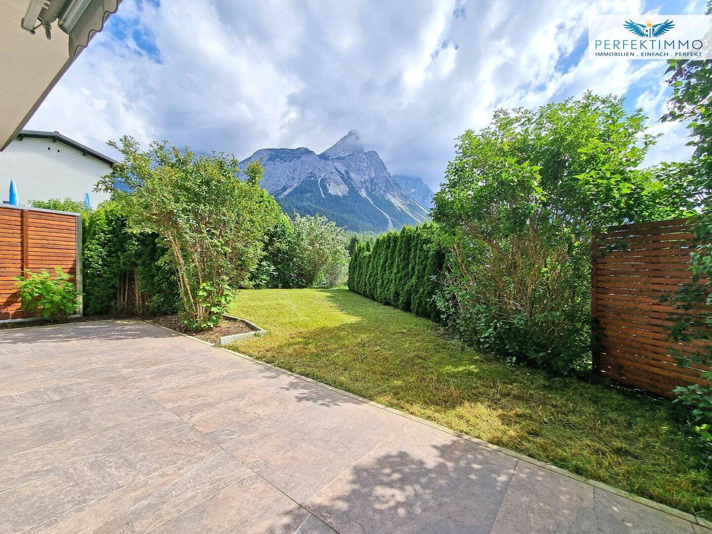 Gepflegter Gartenbereich mit Terrasse, Hecken und beeindruckendem Bergblick.