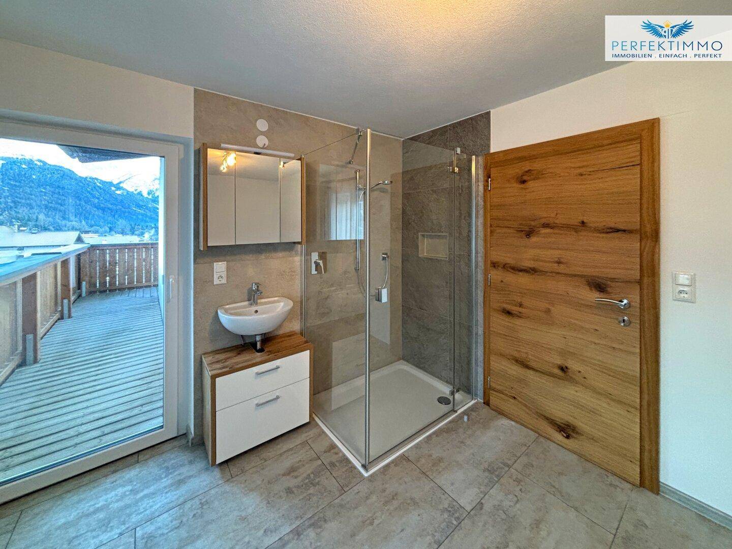 Kleines Badezimmer mit Dusche, Einzelwaschbecken und Zugang zu einem Balkon.