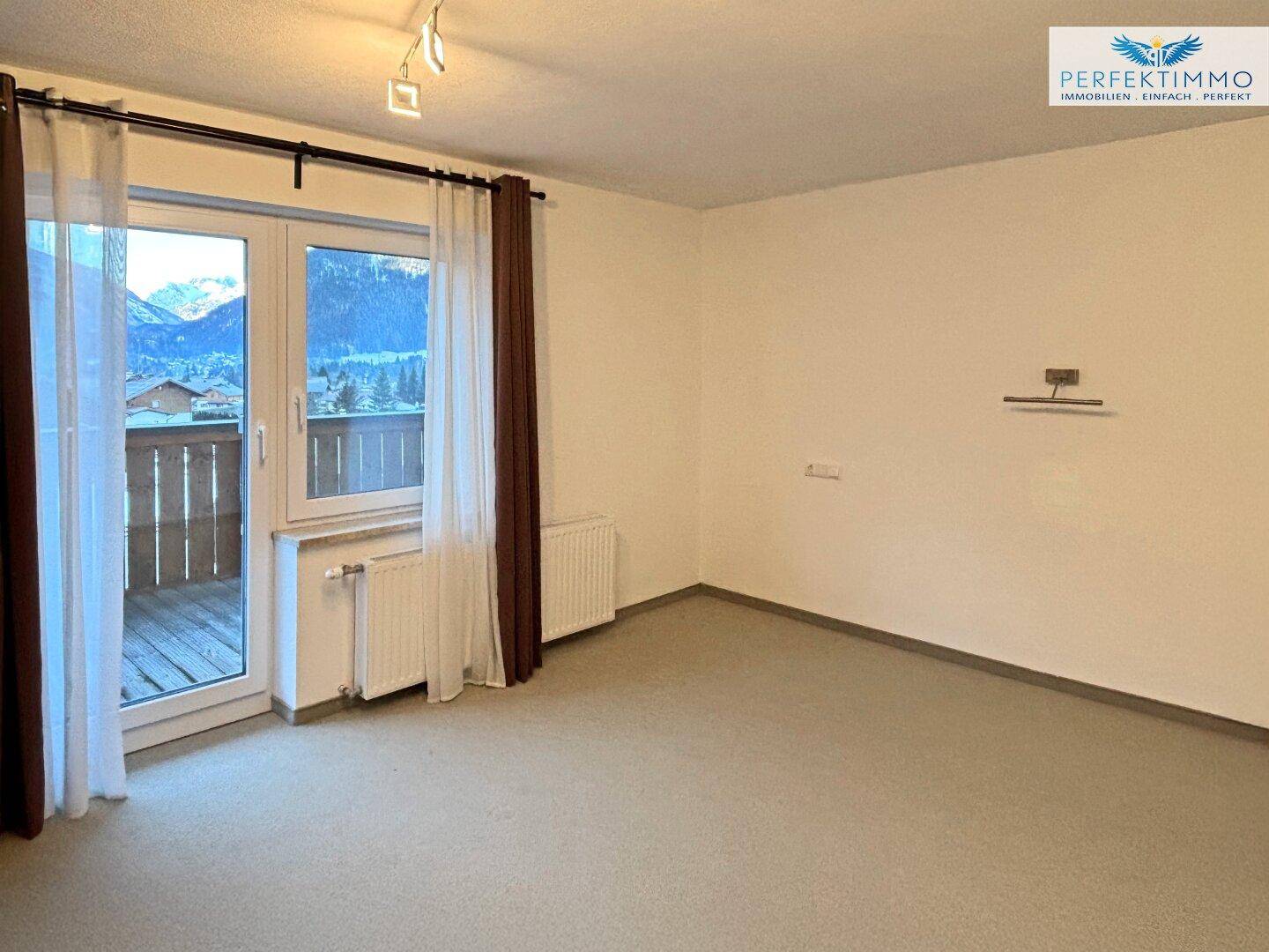 Helles Zimmer mit Balkonzugang und Blick auf die umliegende Bergwelt.