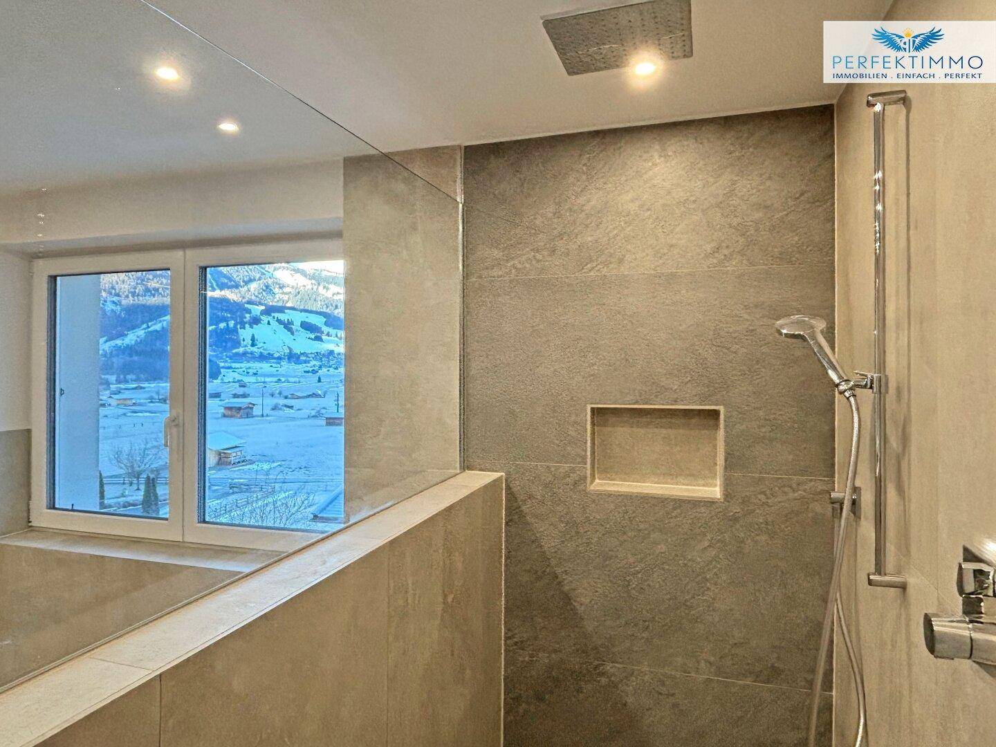 Moderner Duschbereich mit Regendusche und Blick auf die verschneite Berglandschaft.