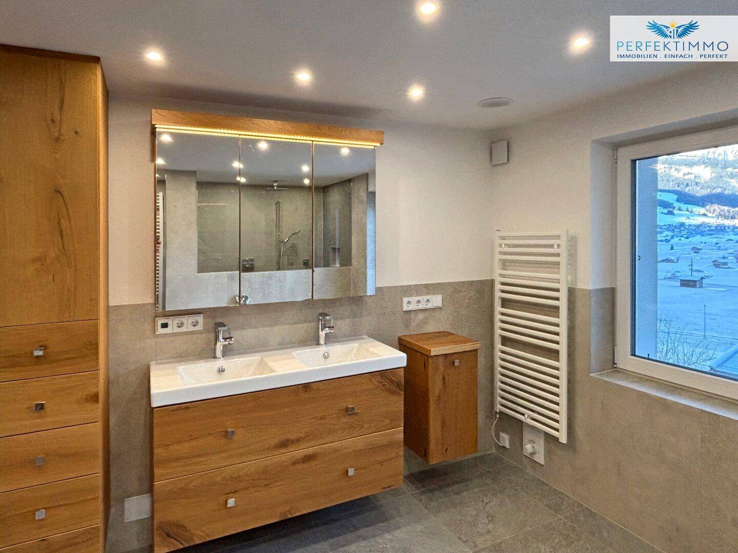 Modernes Badezimmer mit Doppelwaschbecken, Holzmöbeln und Fenster mit Bergblick.