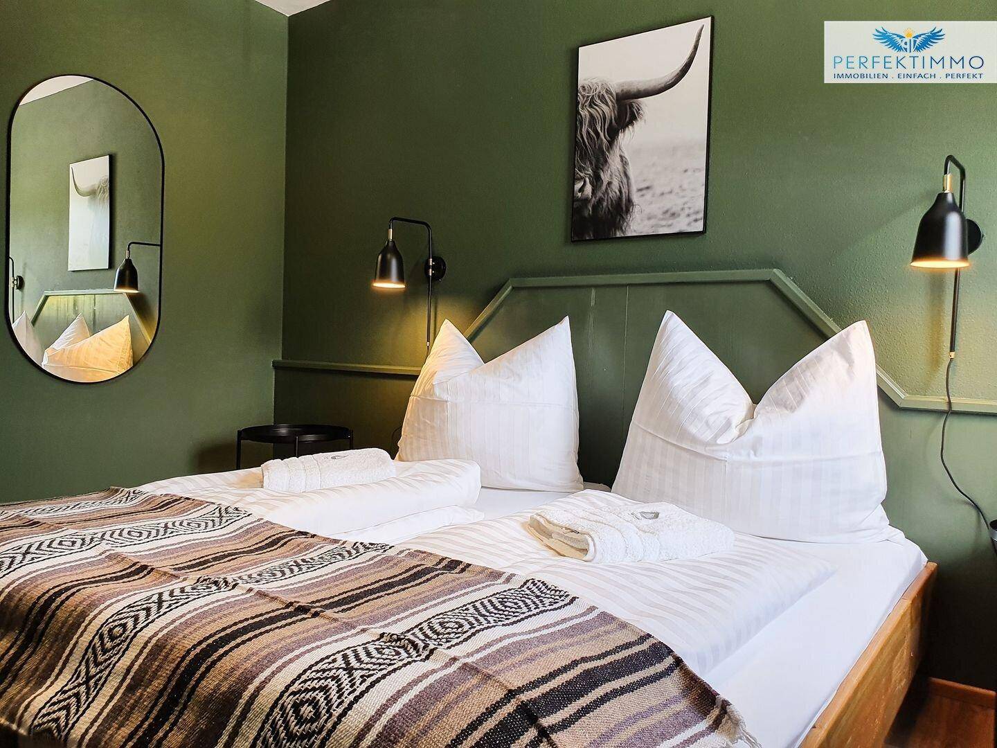 Helles Schlafzimmer mit grünen Wänden, Holzbett und modernem Spiegel.