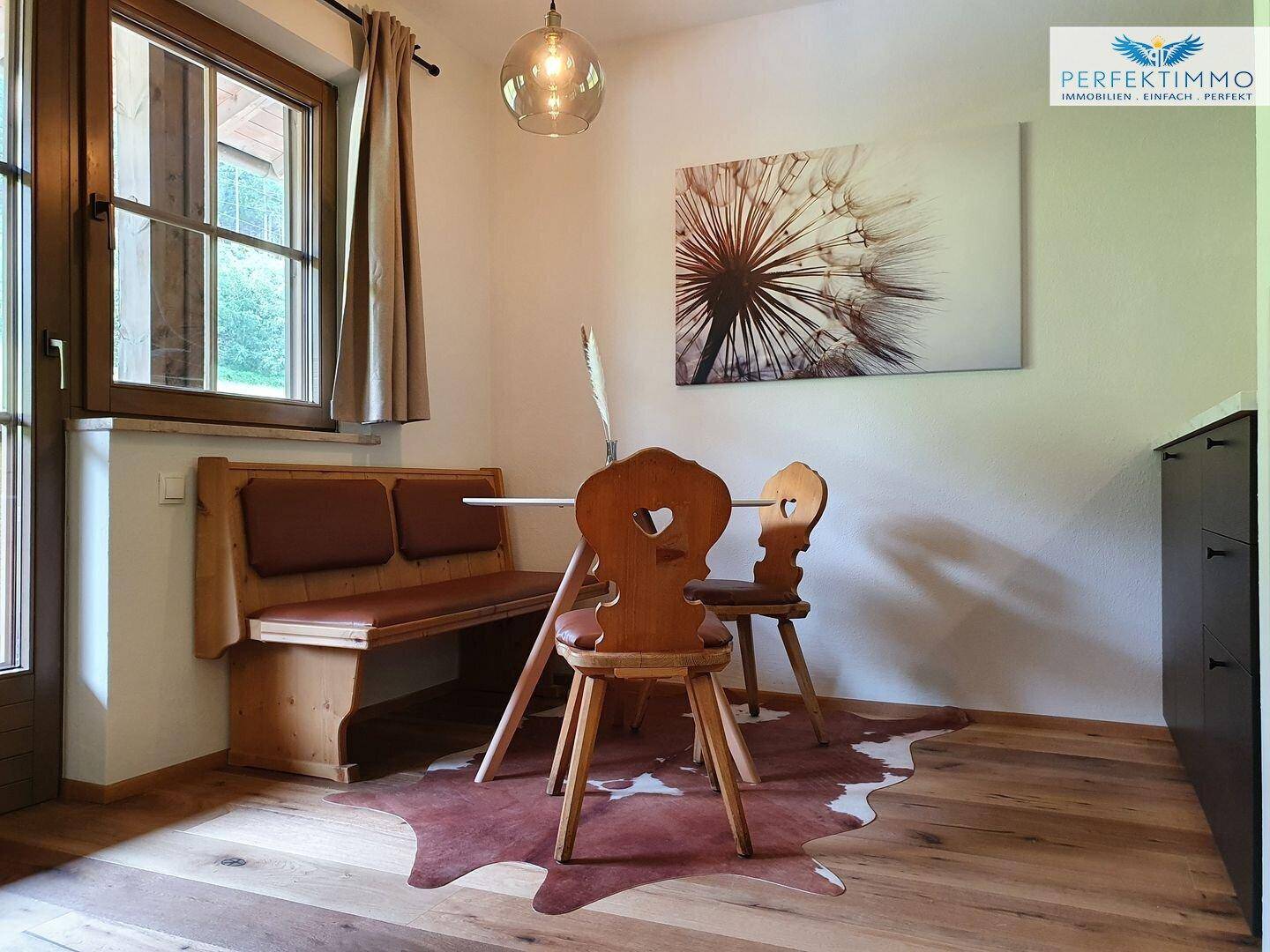Rustikaler Essbereich mit Holztisch, Bank und Stühlen am Fenster.