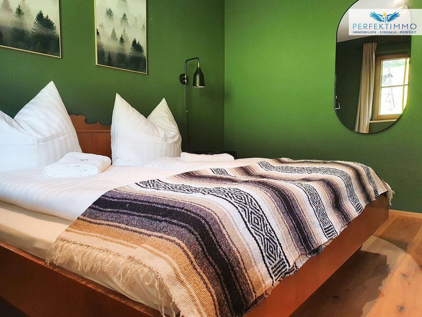 Schlafzimmer mit Holzbett, grünen Wänden und rustikalem Überwurf.