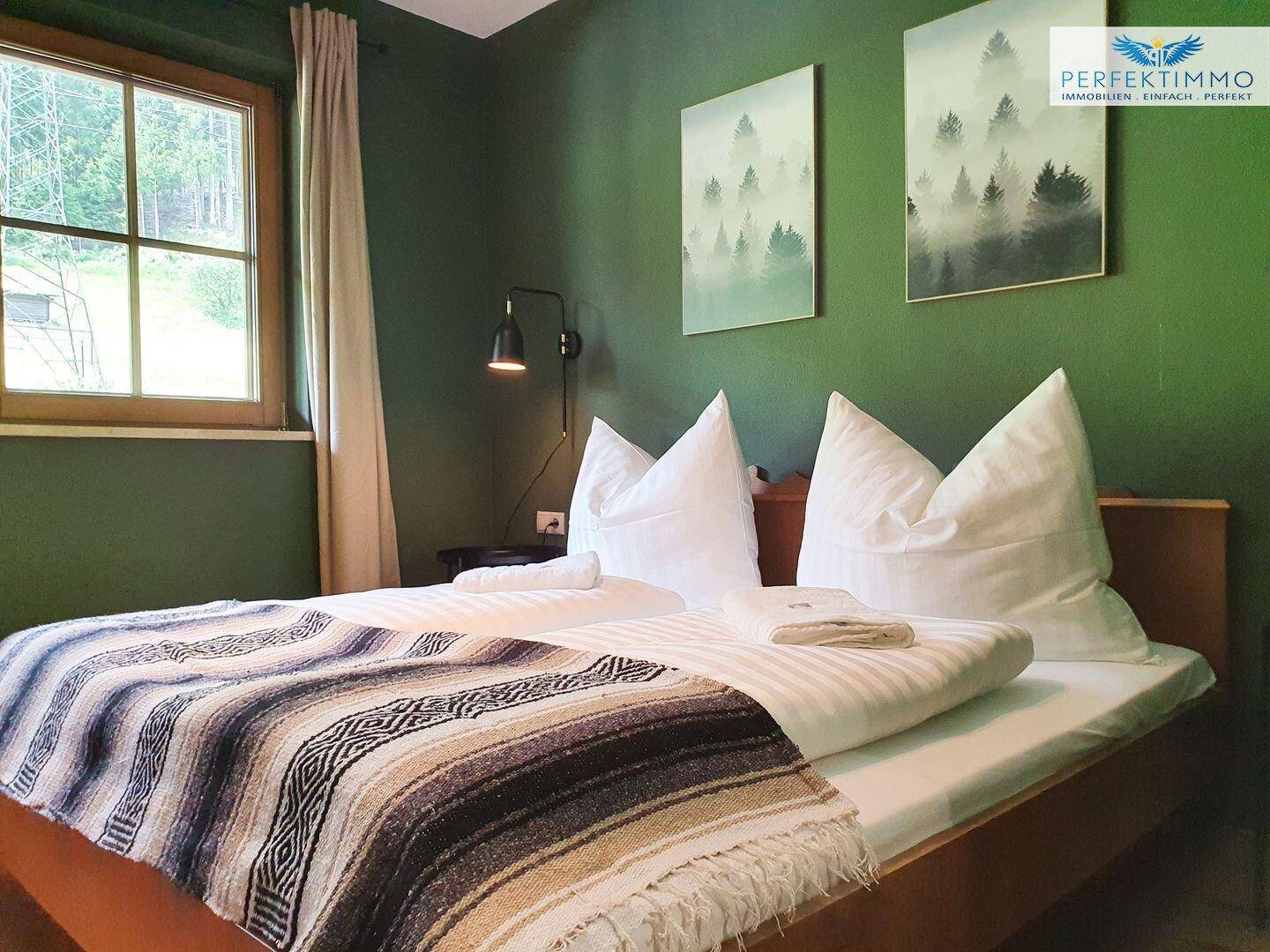 Gemütliches Schlafzimmer mit grünen Wänden, Holzbett und Waldmotiven.
