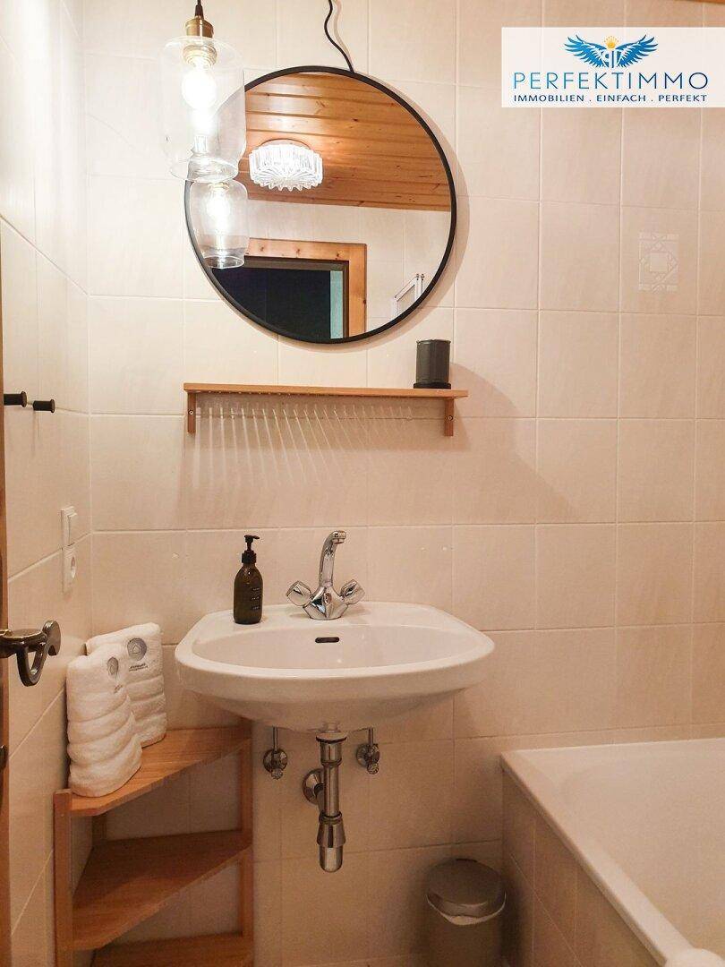 Badezimmer mit Waschbecken, Badewanne und runden Spiegel über Holzregal.