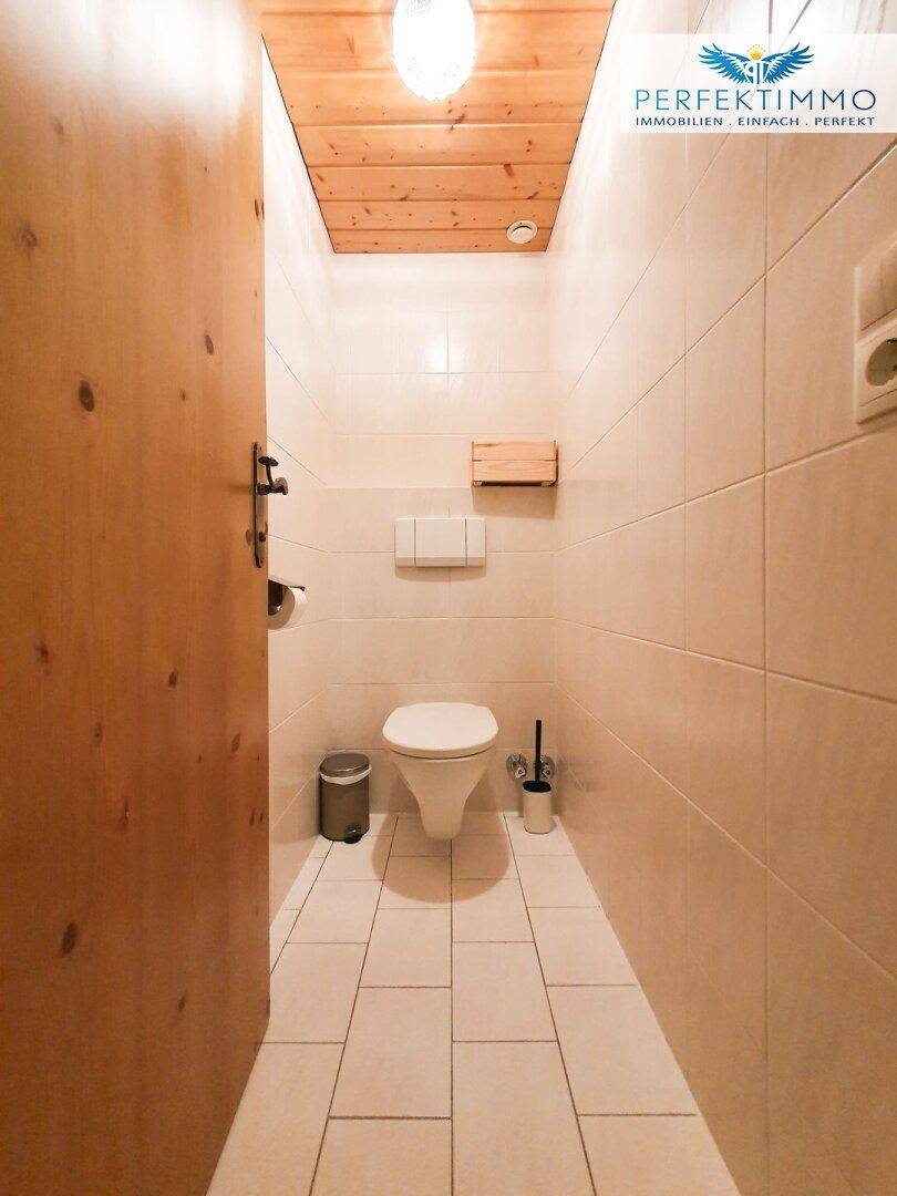 Separates WC mit Wand-WC, hellen Fliesen und Holzdecke.