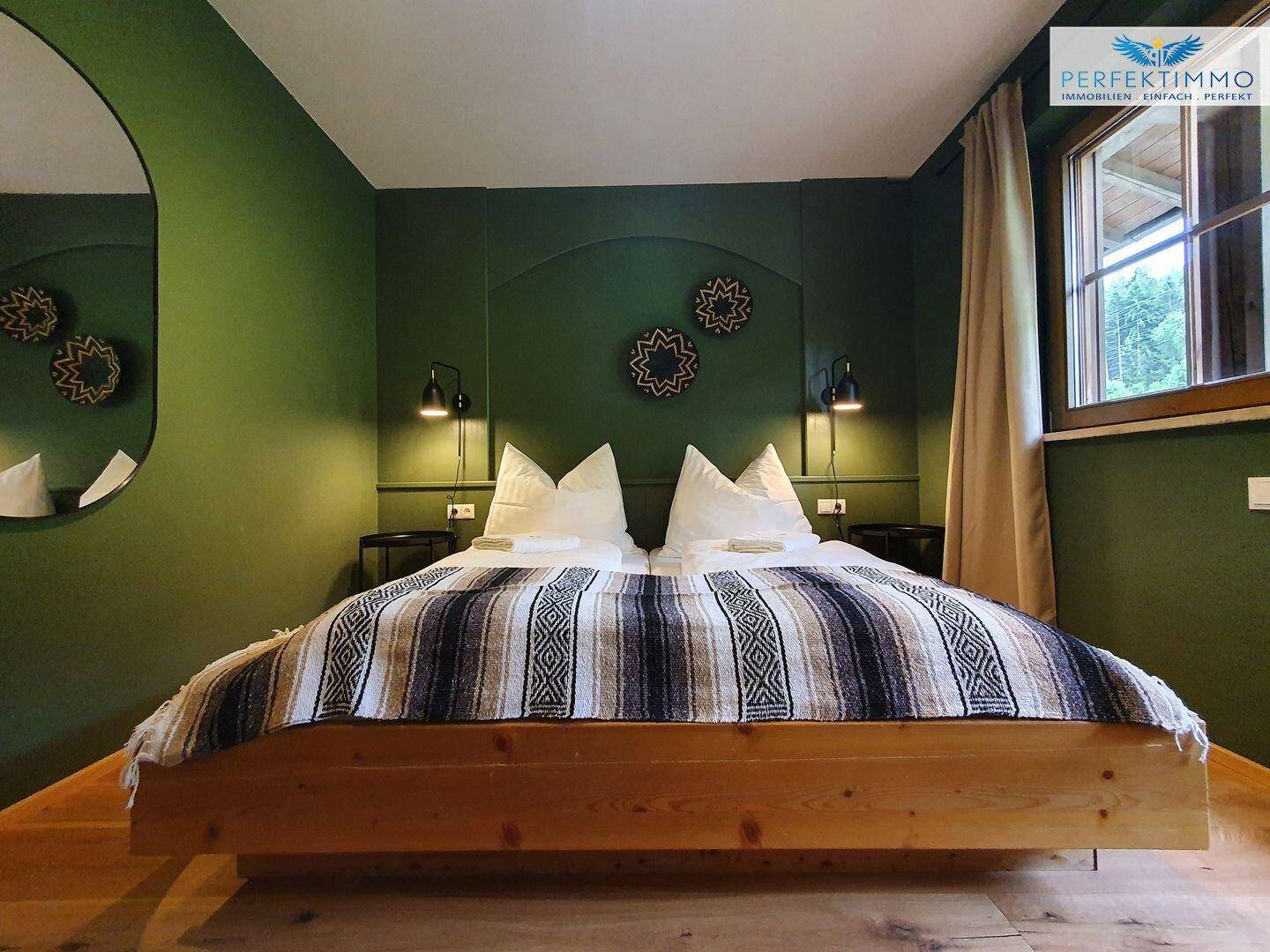 Geräumiges Schlafzimmer mit Holzbett, grünen Wänden und dekorativen Elementen.