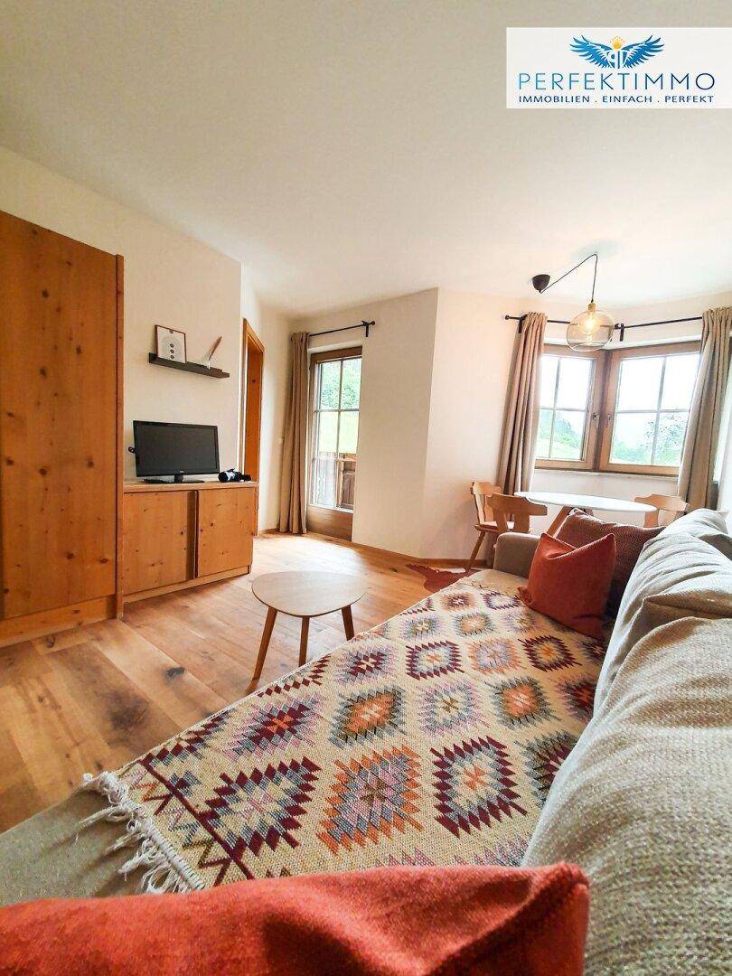 Heller Wohn- und Essbereich mit Sofa, Holzboden und Fenstern mit Ausblick.