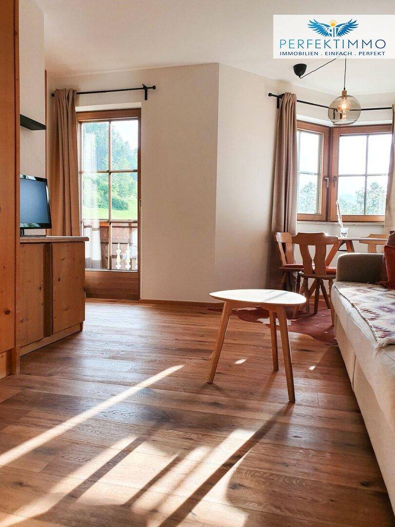 Heller Wohn- und Essbereich mit Holzboden, großen Fenstern und Zugang zum Balkon.