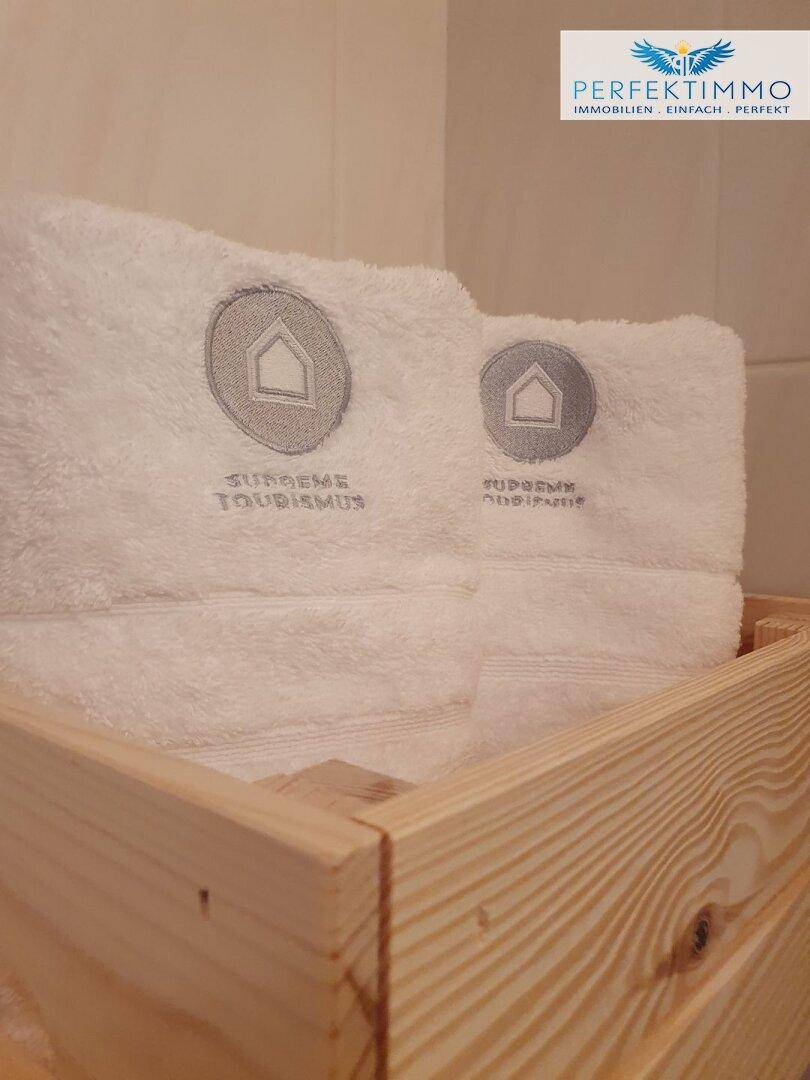 Gestapelte weiße Handtücher mit Logo in einer Holzkiste, bereit zur Nutzung.